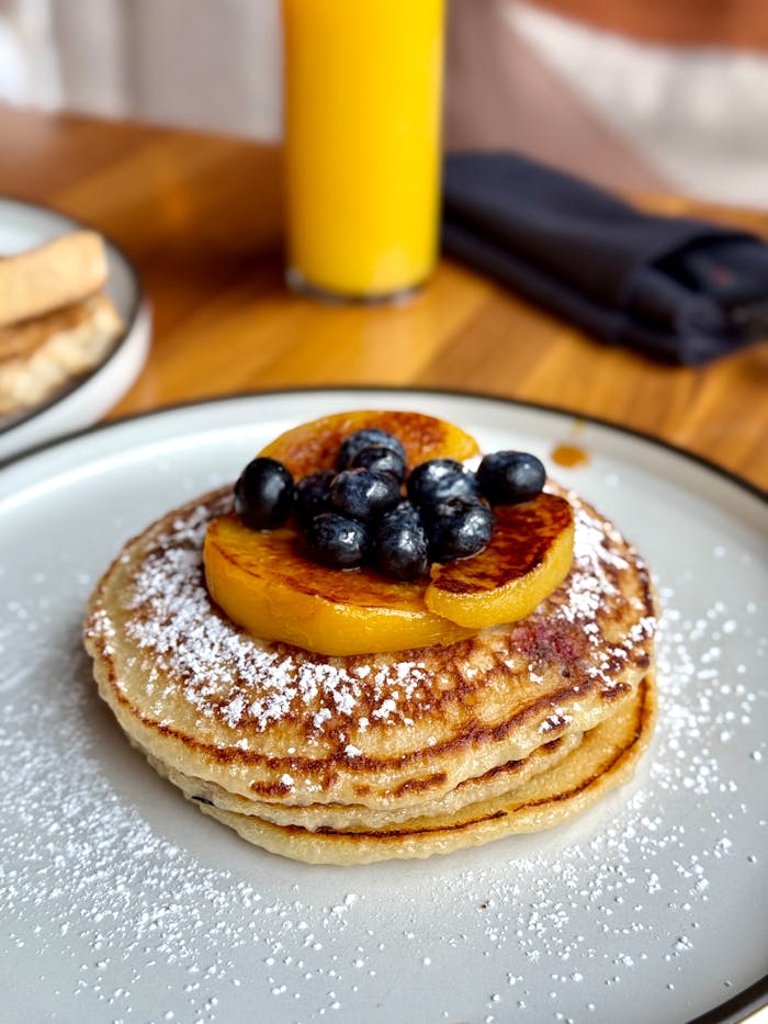 Mouth-watering pancakes topped with blueberries, orange slices, and powdered sugar, perfect for breakfast.
